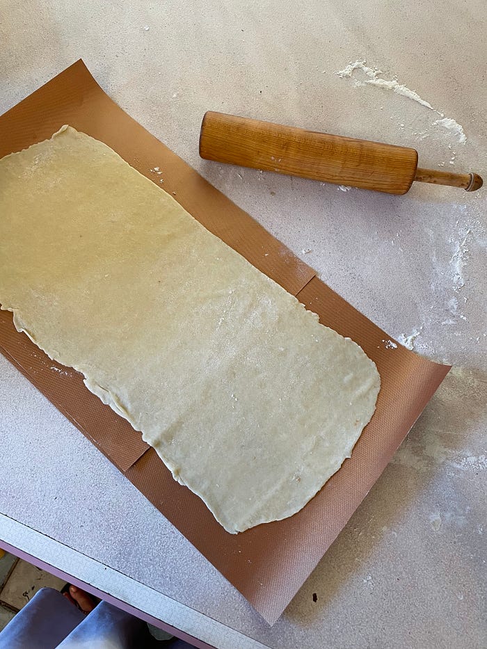 Rolled out pastry dough on a wax mat next to a rolling pin.