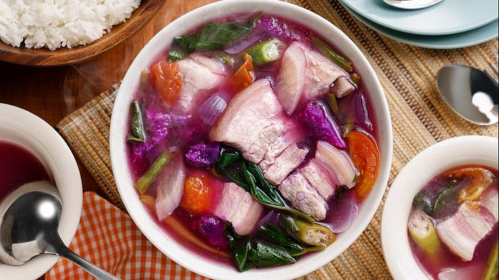 A bowl of savory soup with pork, tomatoes, onions and greens