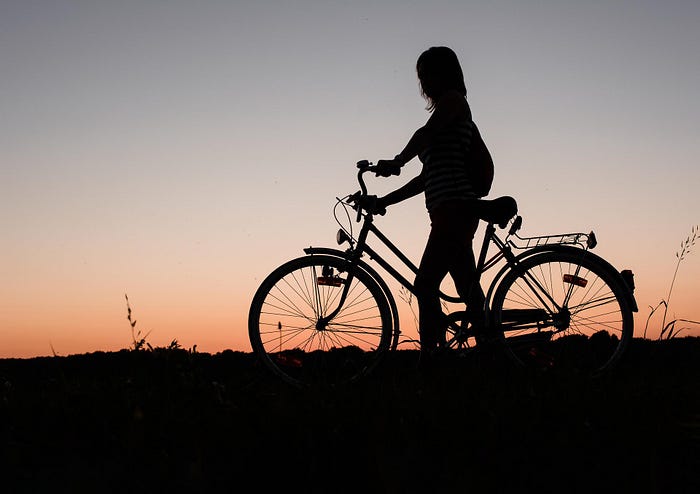 Silhouette photo of girl standing next to bike, at dusk