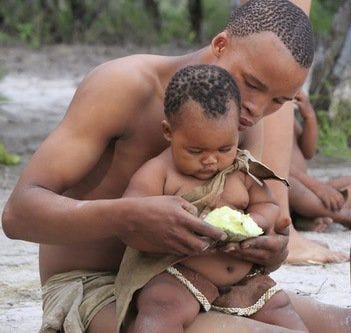 A male Bushman of the Kalahari holding and feeding a small child