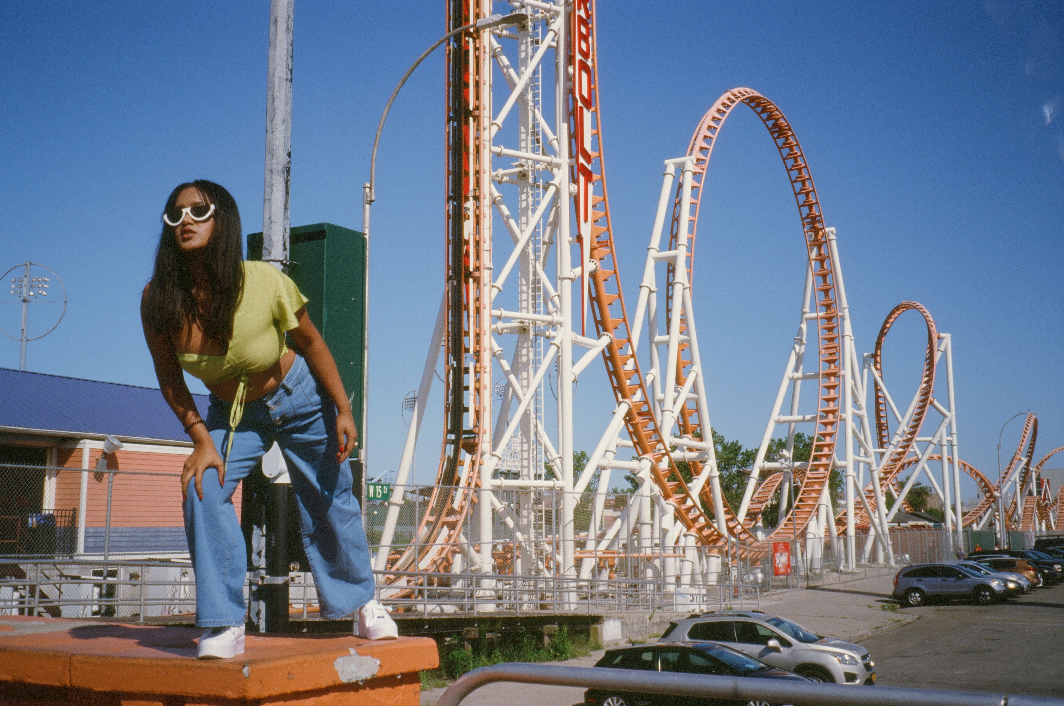 A woman in shades strikes a pose in front of a classic loop-the-loop rollercoaster