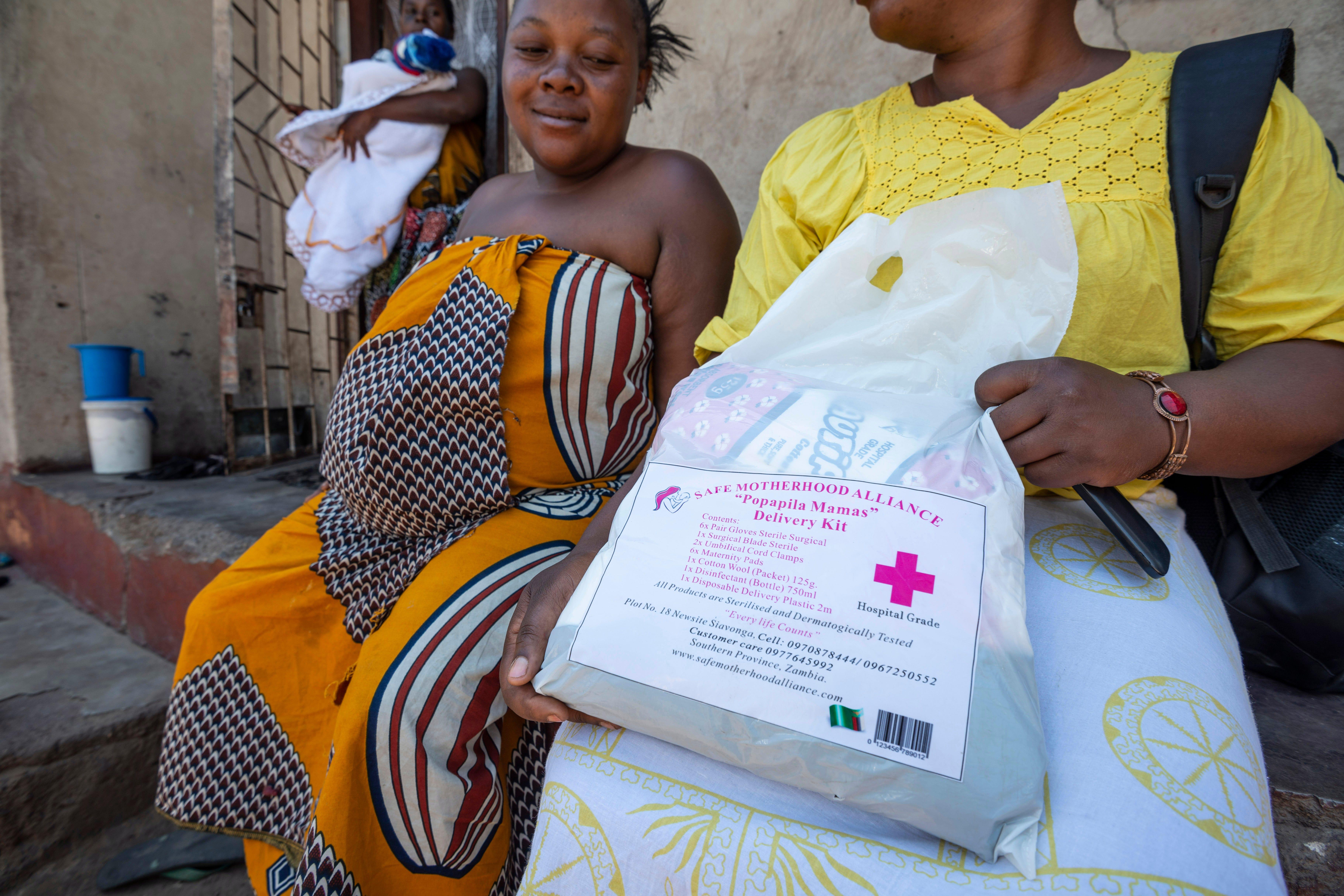 Two women sitting.  One holding bag containing baby delivery kit.  Image credit: Safe Motherhood Alliance