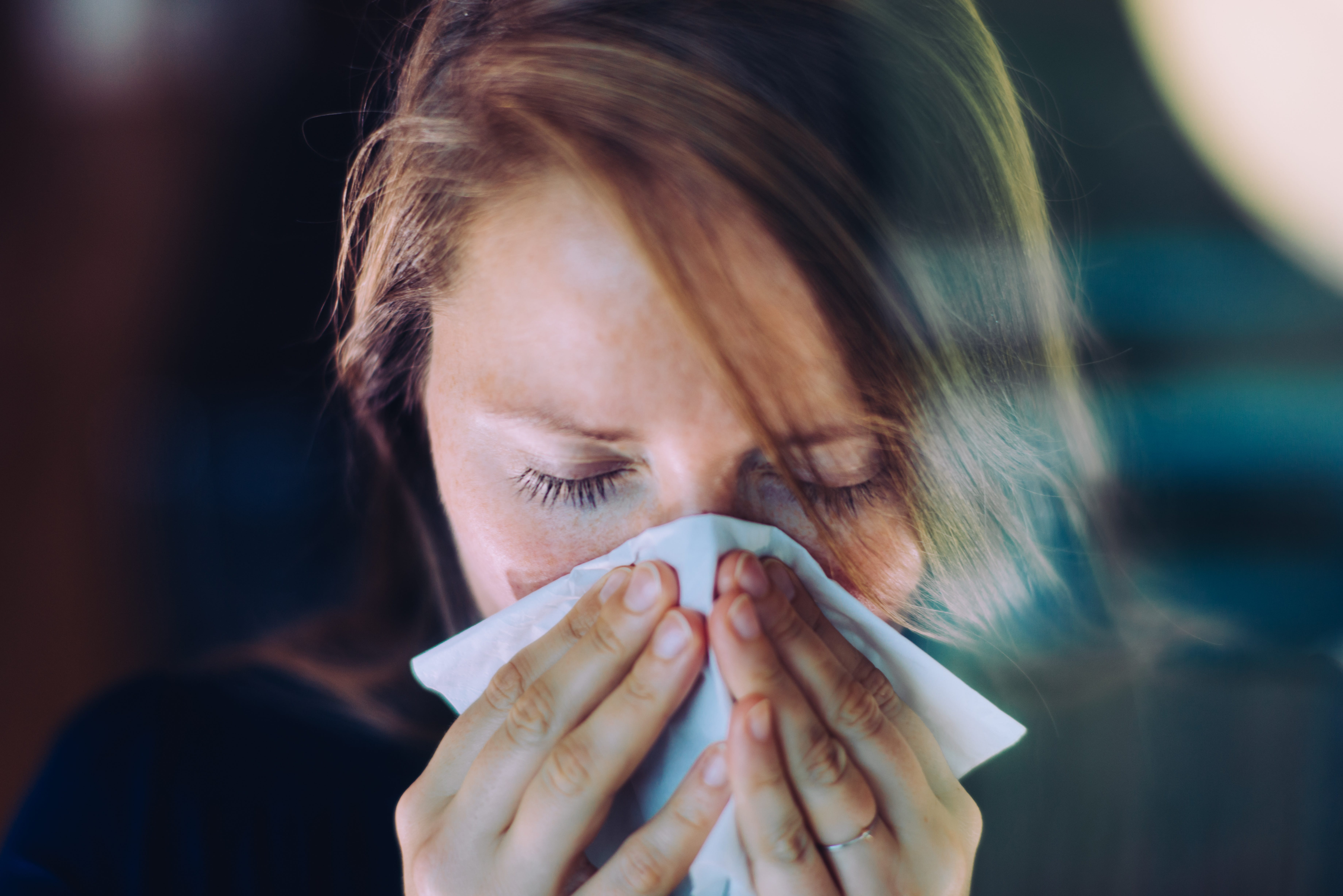 Woman sneezing behind a window, using a tissue.