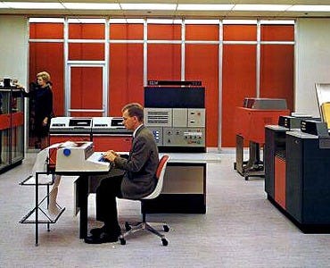 Two people are operating large computers and mainframes. Image from the IBM archives.