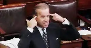 A picture of Congressman Biden, a bit darker hair, dark suit, and tie on the Congress floor. He’s scowling, teeth bared, and holding an index finger as if a gun to both sides of his own head. Courtesy C-SPAN, 1993