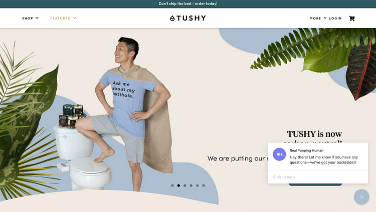 A hero image on Tushy’s home page features a man wearing a superhero-type cape made of a bath towel. His shirt says “Ask me about my butthole,” and he stands triumphantly, smiling into the distance, with one foot up on the toilet. A collage of leaves surrounds him. A live chat feature, labeled “Real Pooping Human,” offers to answer the user’s questions.