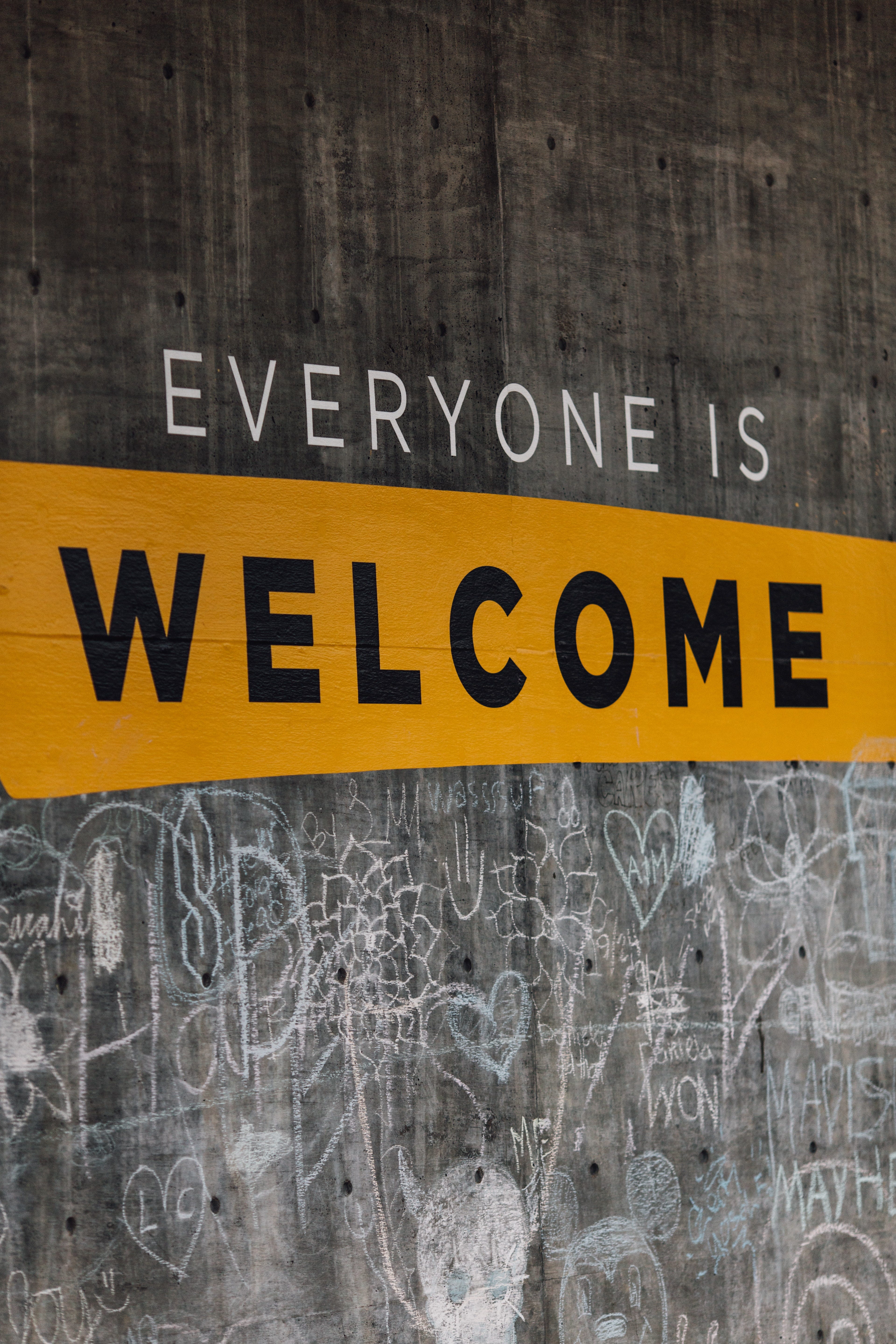 Sign on concrete wall with graffiti “Everyone is welcome”