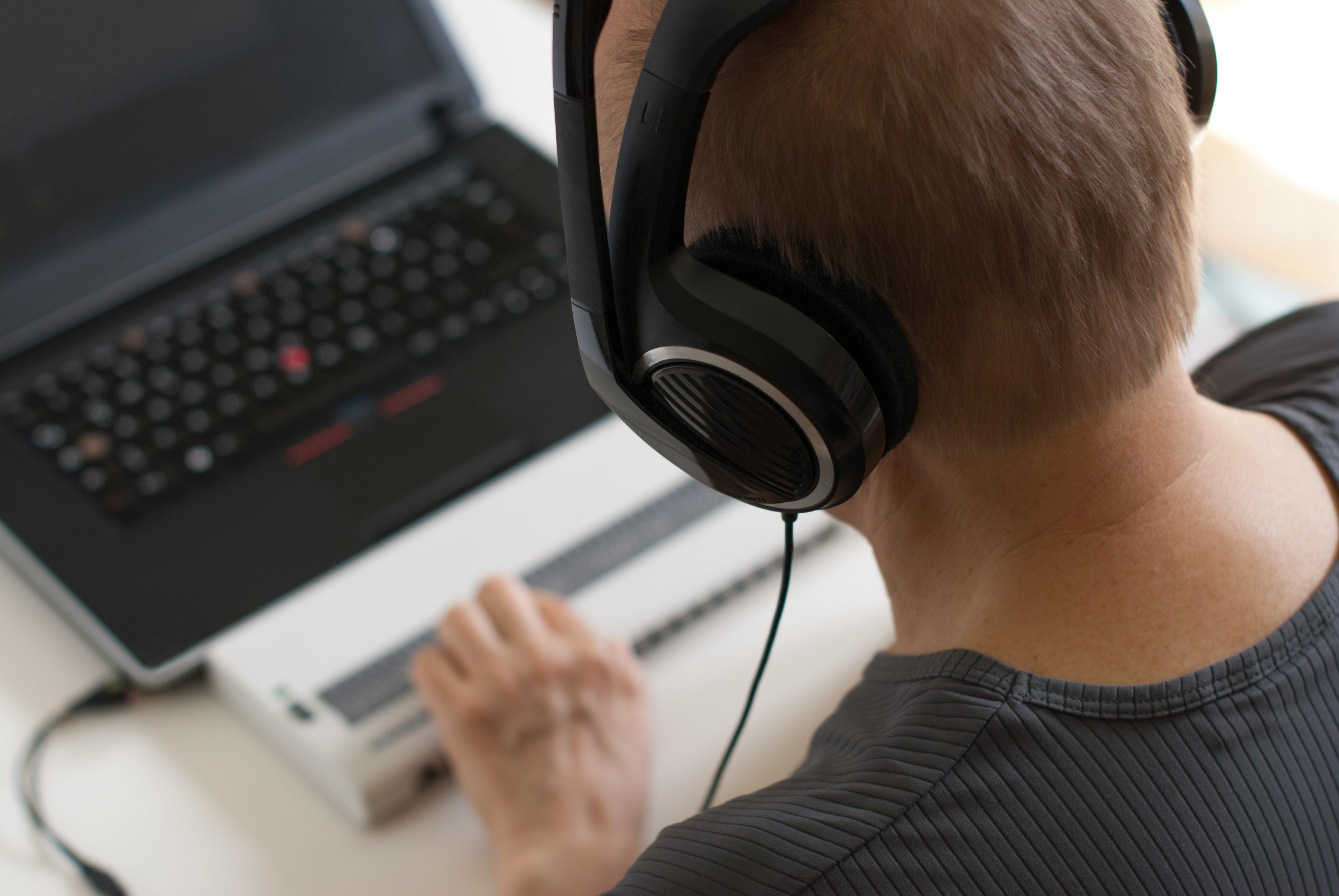 Man wearing headphones with laptop in front of him with hands on refreshable Braille display