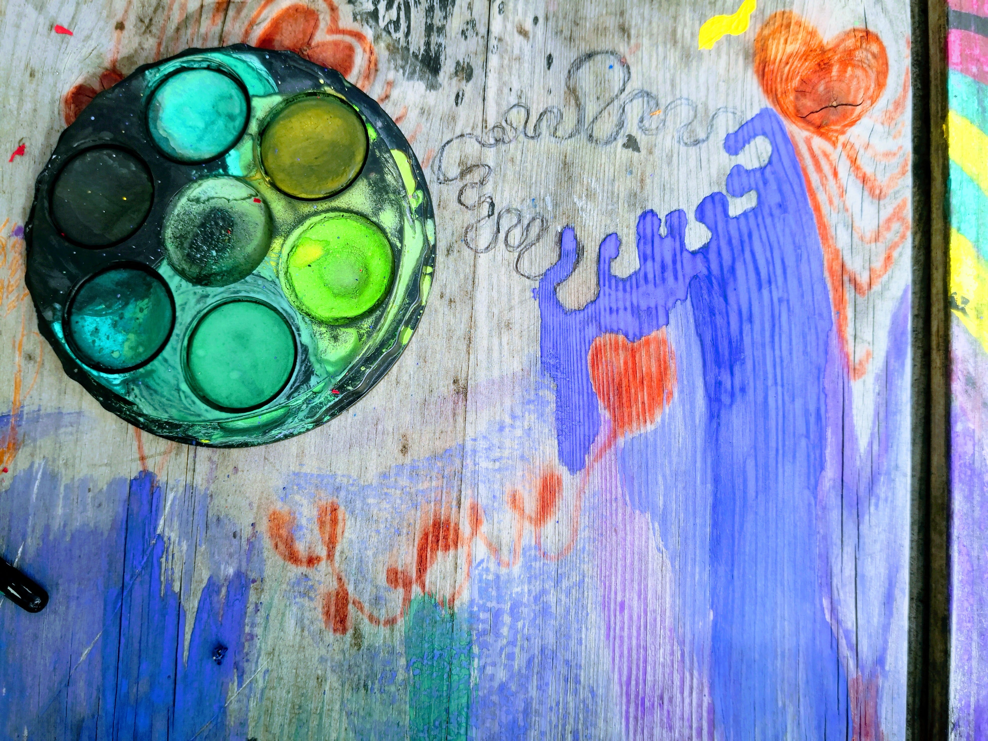 Paint pallet on wooden table covered with colourful paintings and doodles