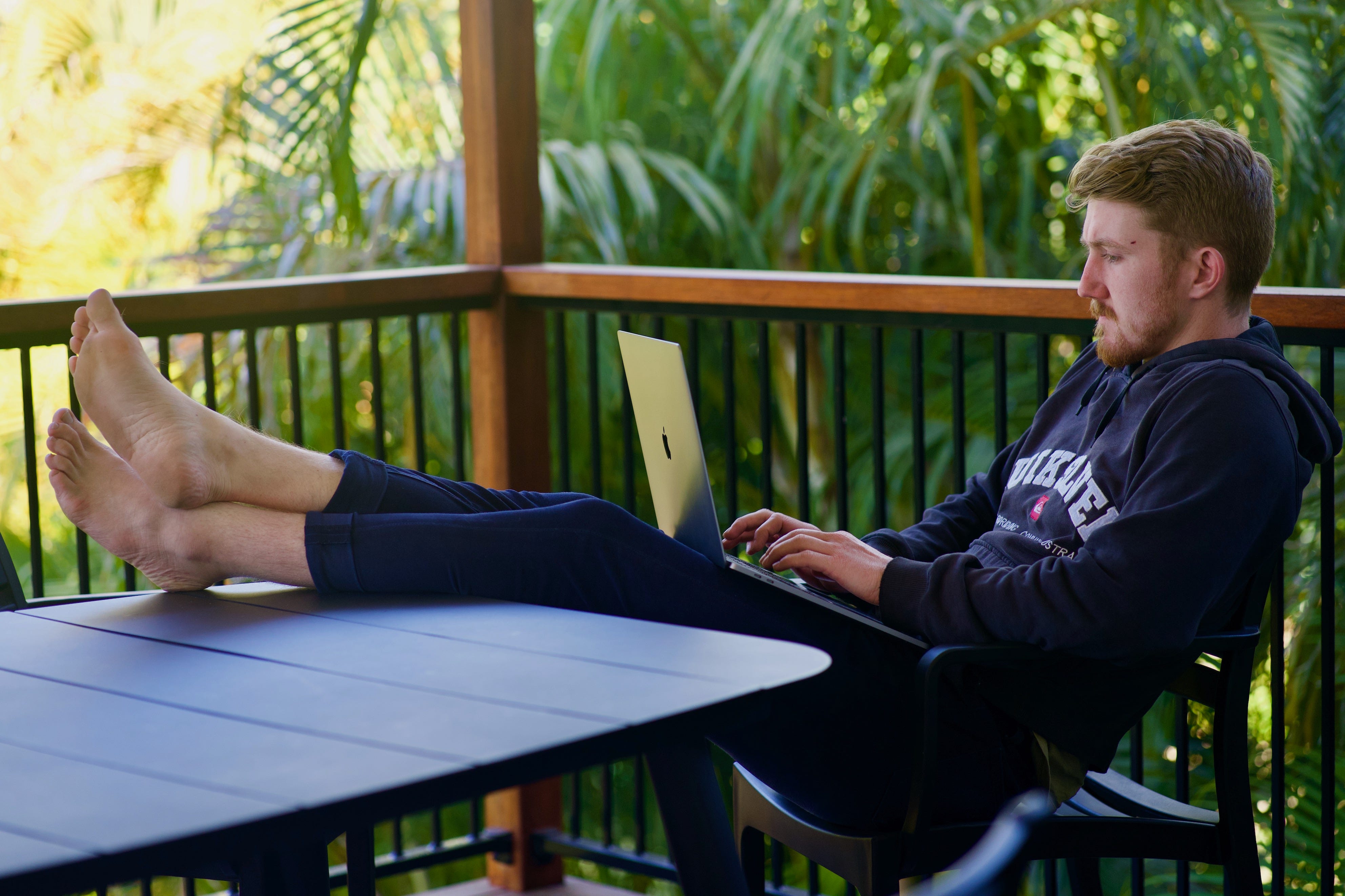 man writing on laptop with feet up on table sitting amongst trees