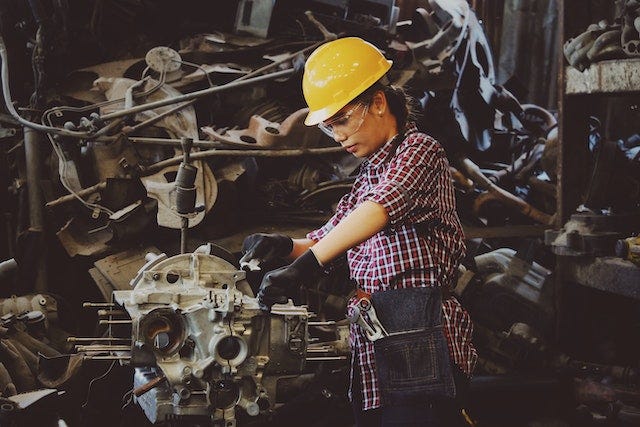 A woman is handling machines, wearing a yellow helmet.