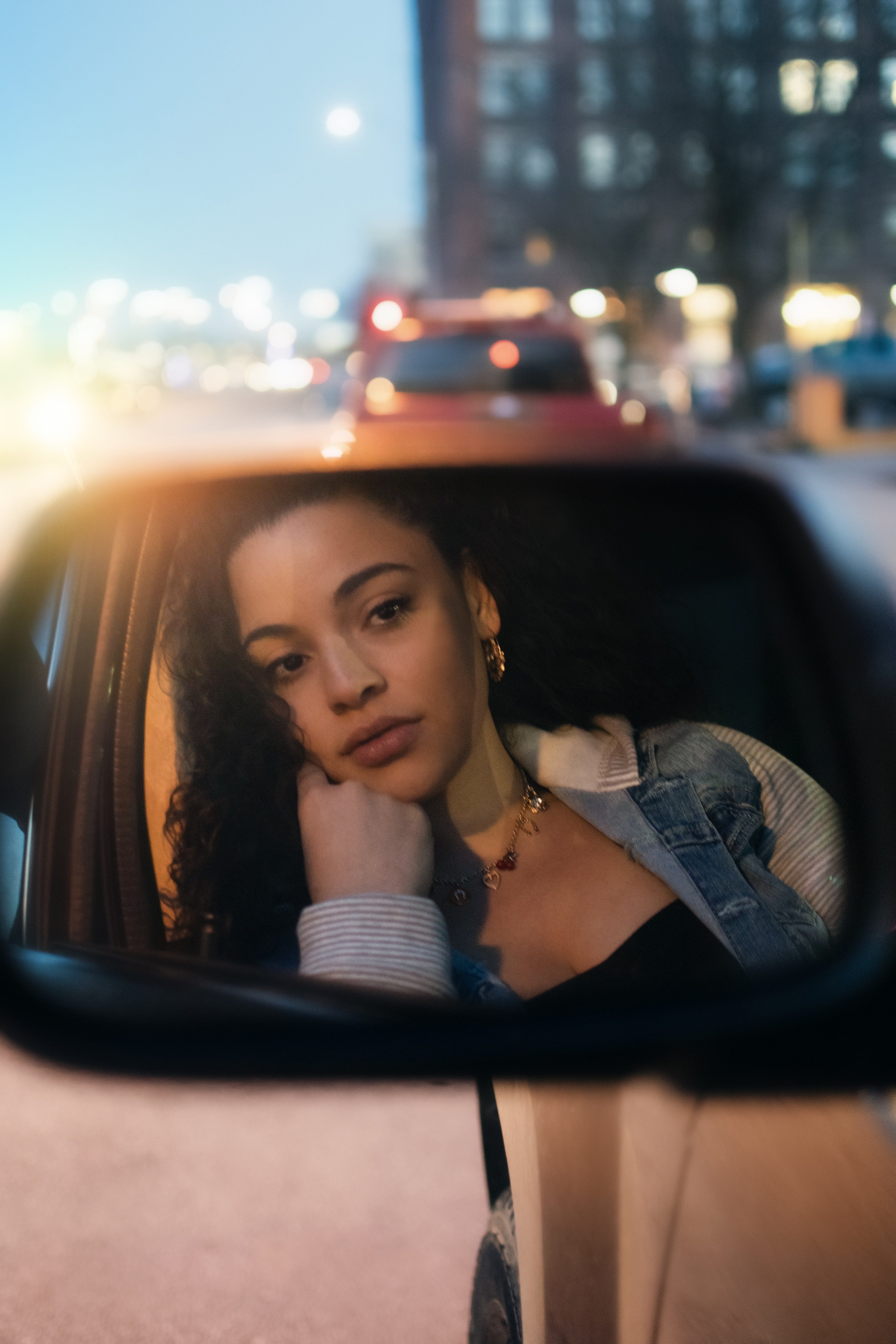 Woman of colour looking pensively at a car mirror