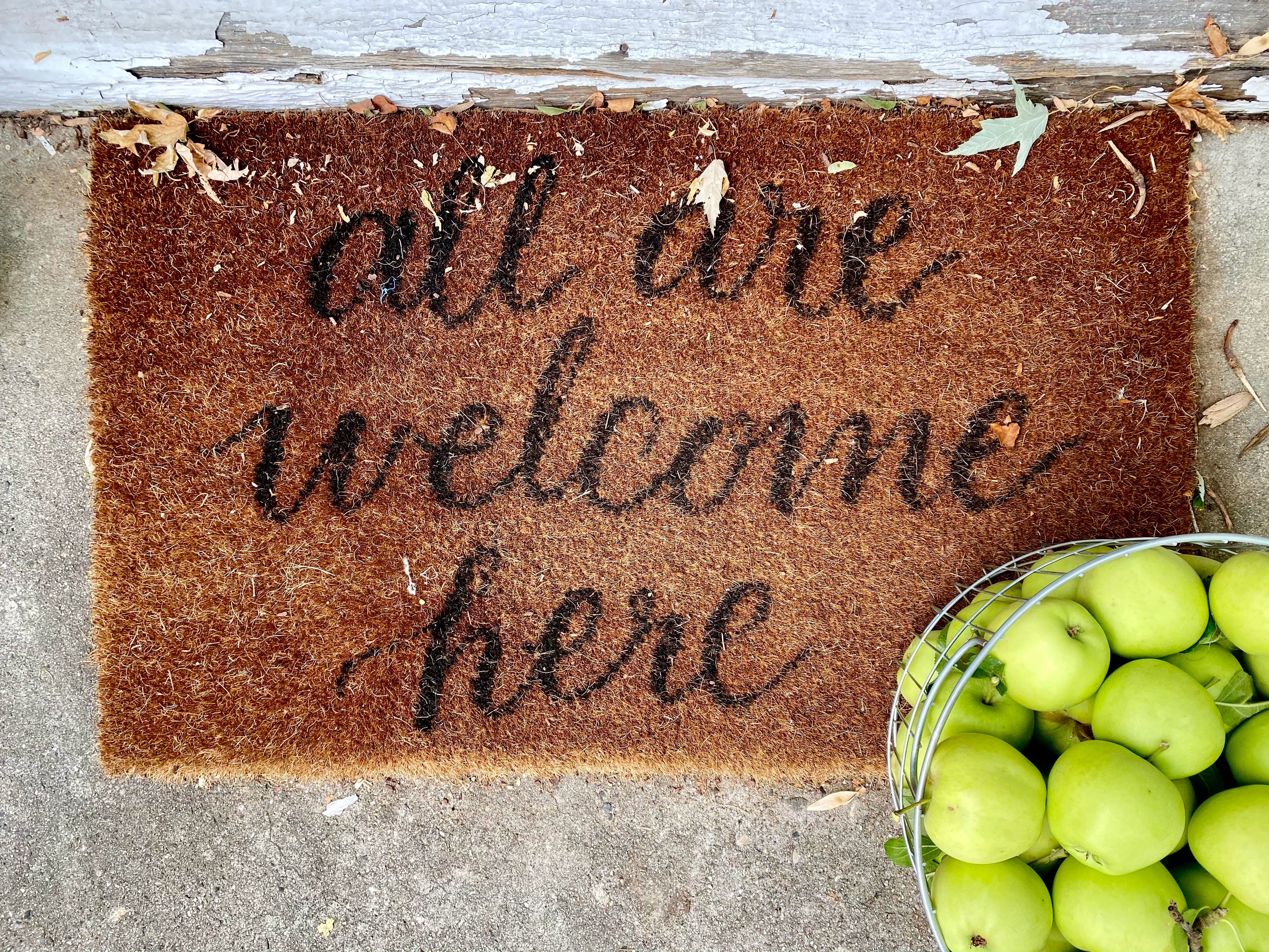 A brown doormat with a black text: ‘all are welcome here’