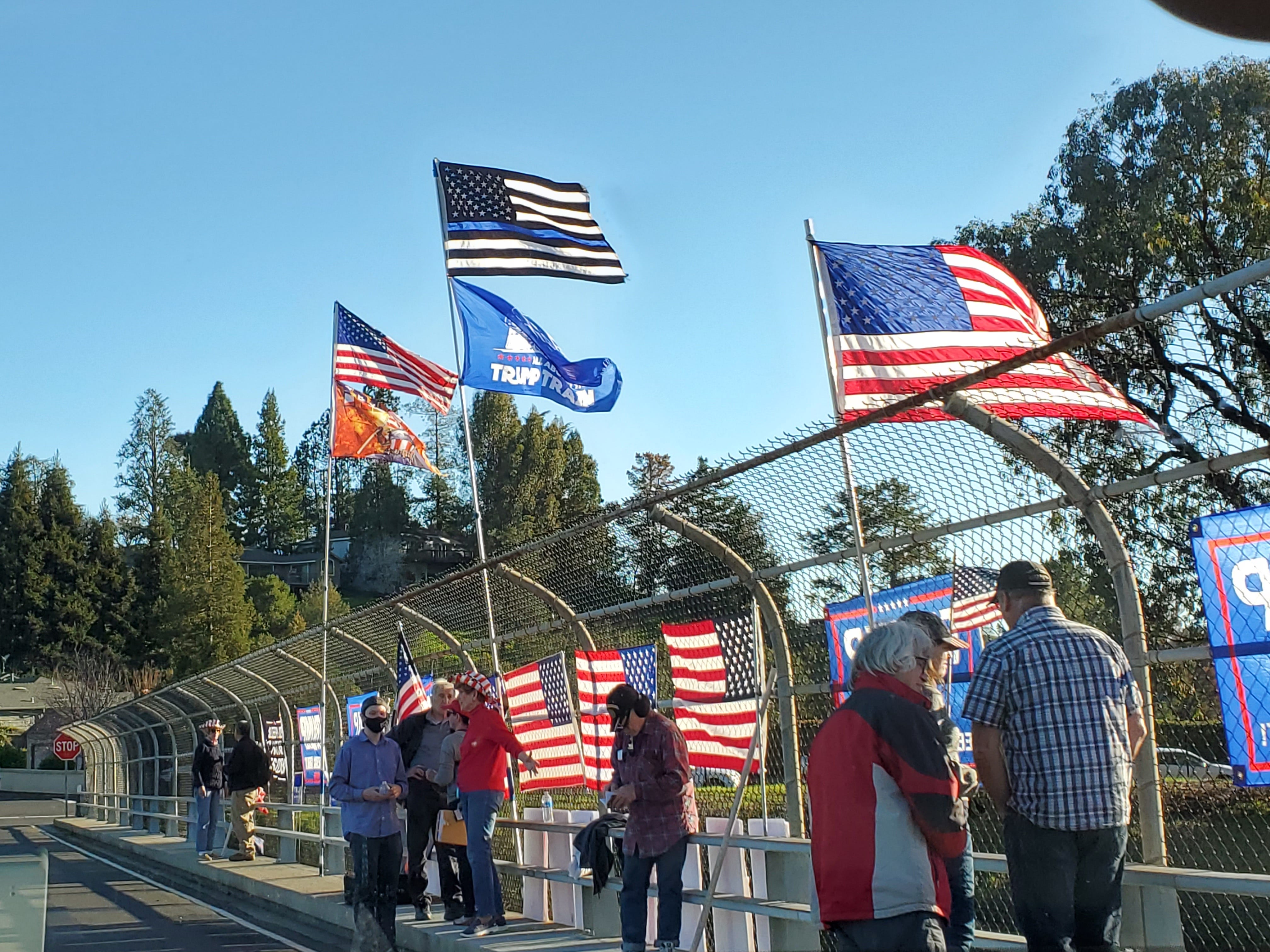 Protesters on a highway overpass flying Trump, Thin Blue Line, and US flags.