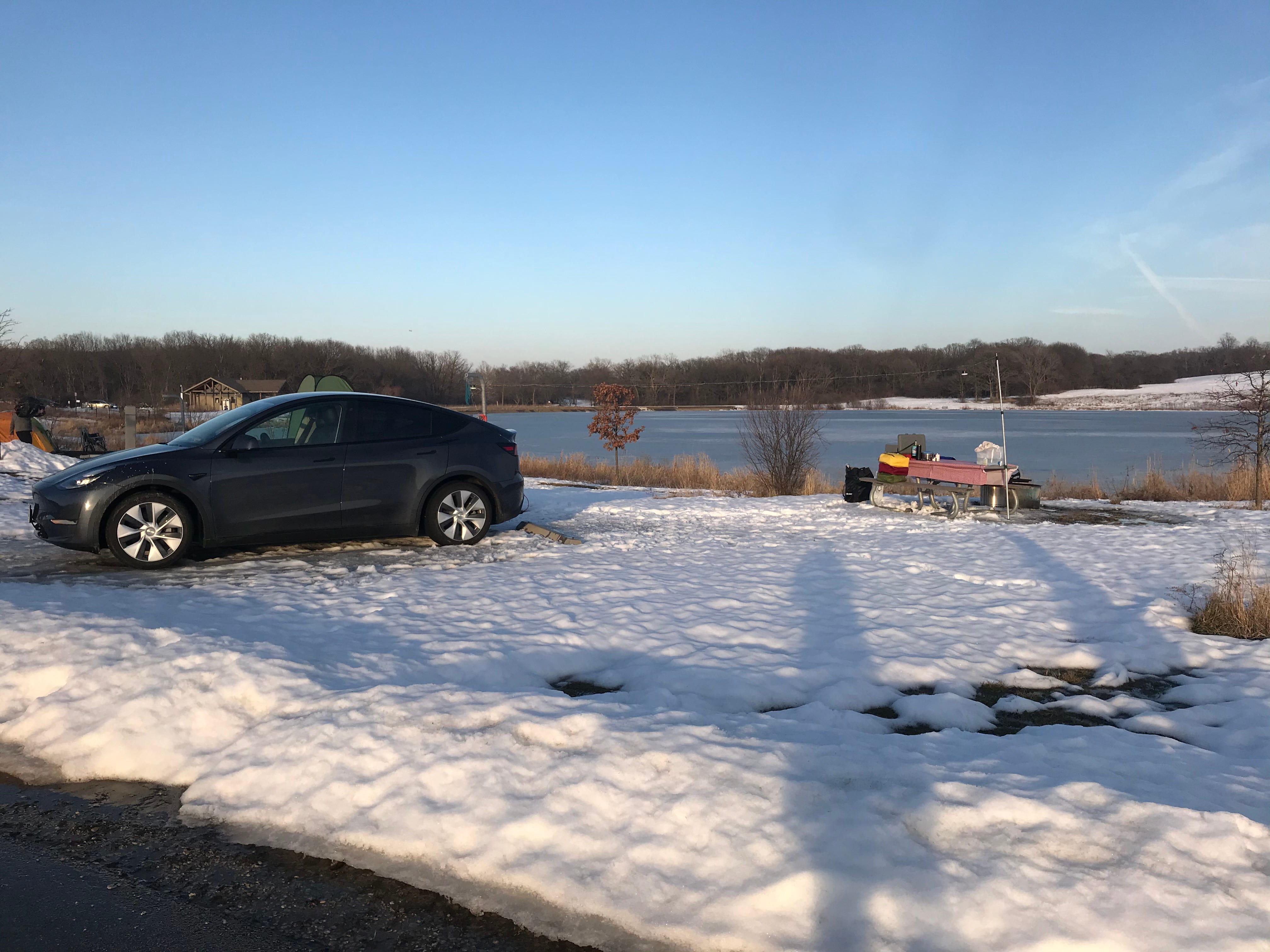 tesla model sits on snow ground in campground near lake