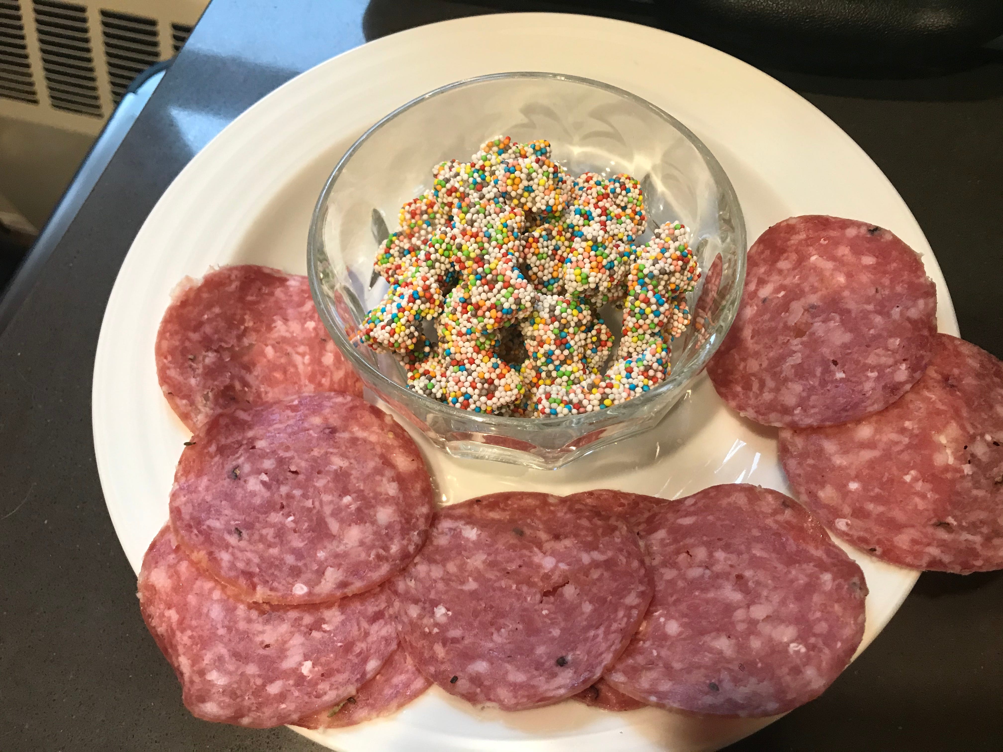 A bowl of sprinkle-covered gummy bears surrounded by slices of salami.