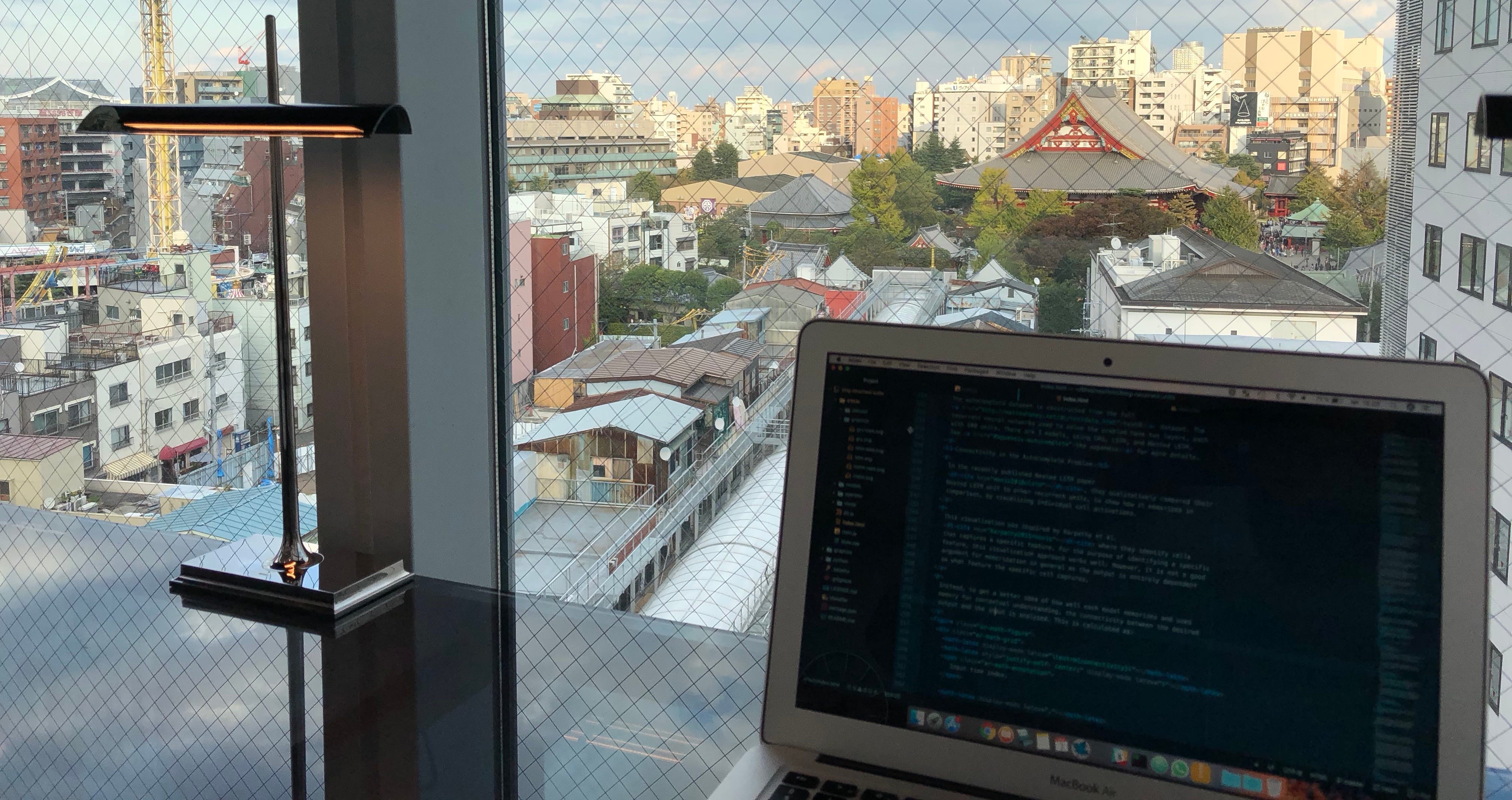Picture of my computer with the HTML code for my distill.pub publication. Background is a window showing Tokyo, Japan.
