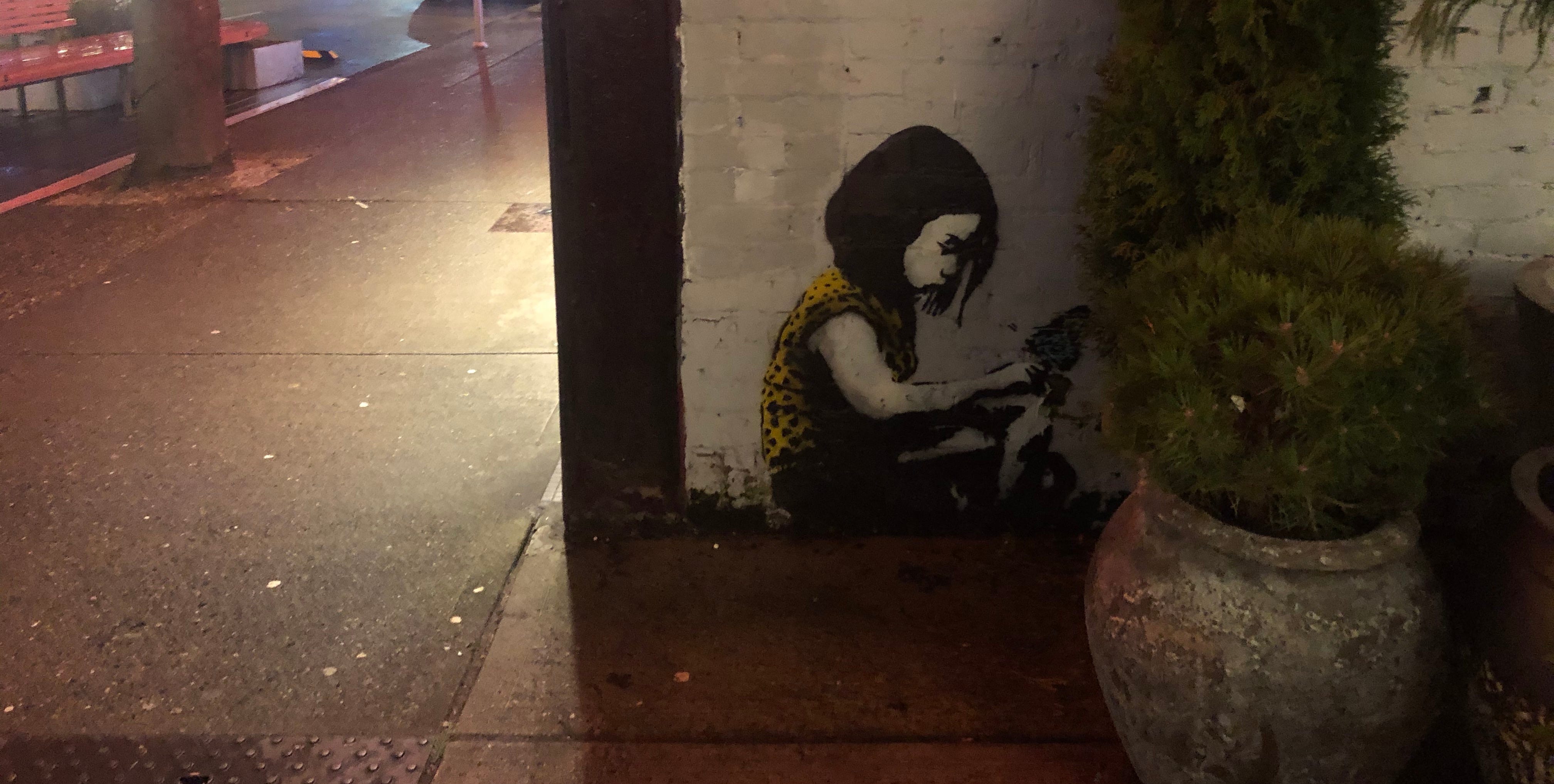 Street art of a girl, sitting in a corner, maybe with a book, looking a bit.