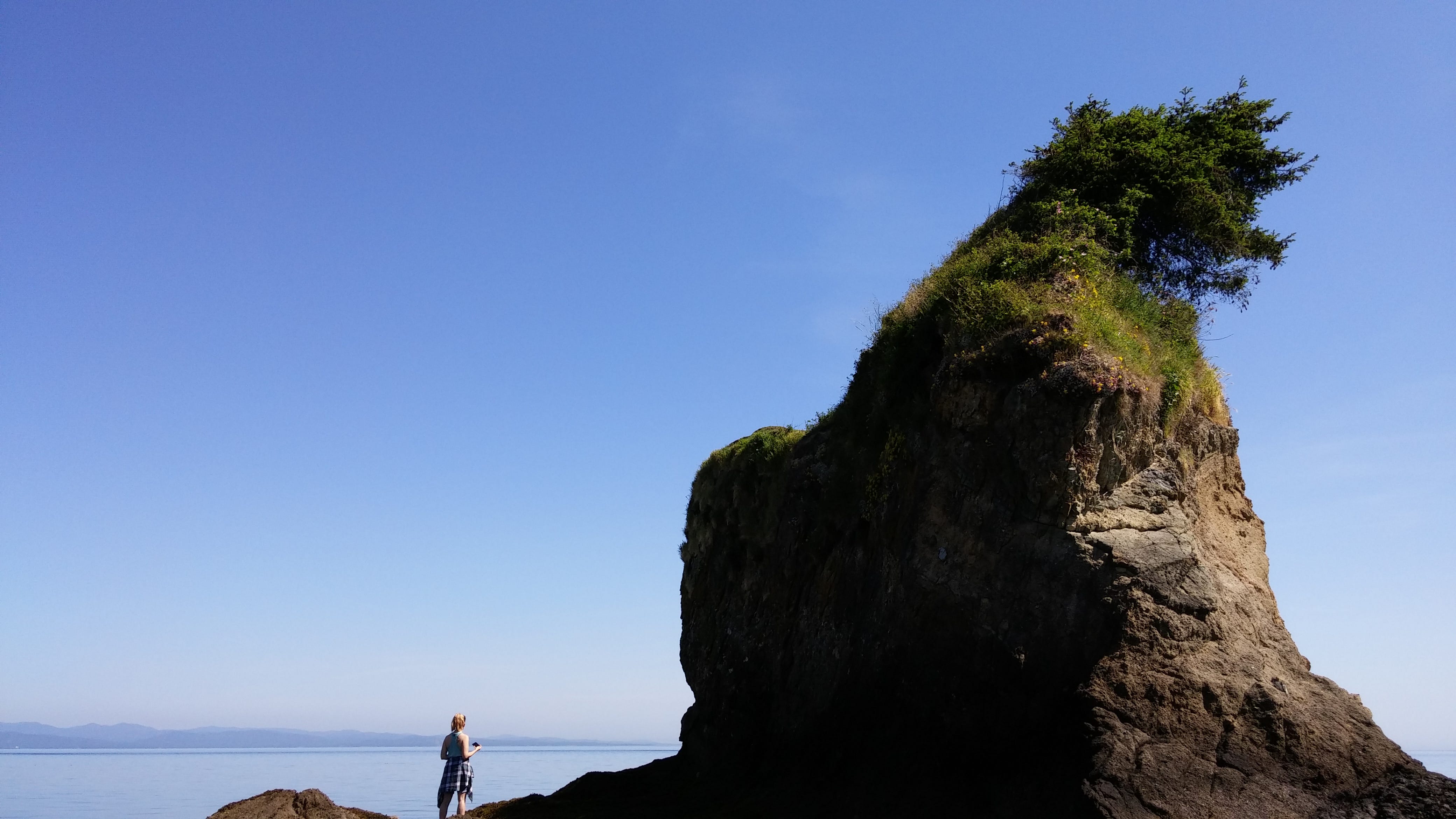A hiker appears tiny in comparison to the sea stack she is standing next to.