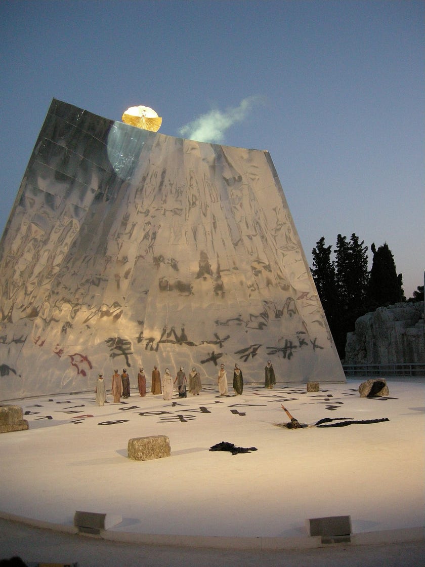 Deus ex machina from Euripides’ Medea (2009, Italy) —The image shows a bunch of people suffering on the ground and looking up towards a God-like blindingly shining being arising from the top of a mountain.