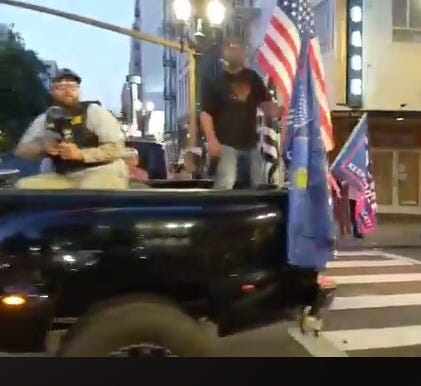 Men holding guns in back of pickup truck with flags