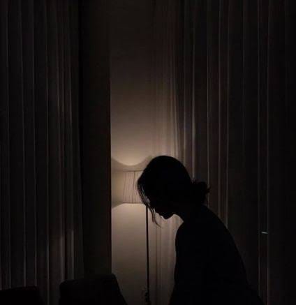 A sad girl in a dark room, sitting by the side of a table lamp.