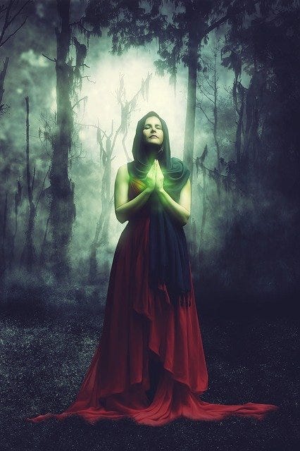 A bewitching female stands in the foreground, dressed in red with black shroud. From her hands in prayer, glows a green orb.