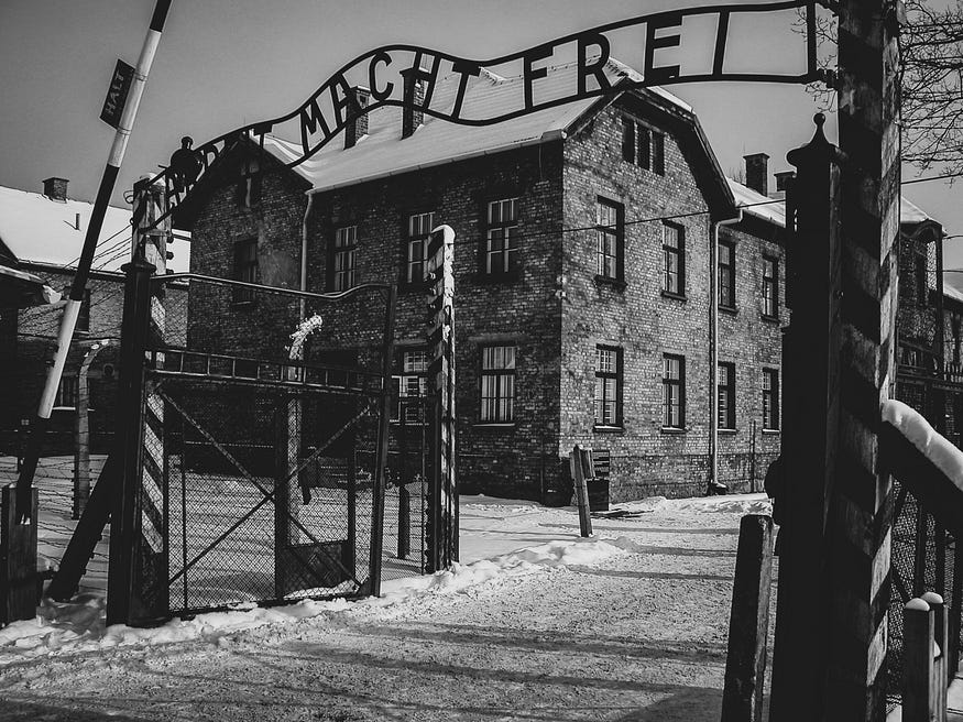 A black and white image of the entrance to concentration camp Auschwitz, with the words ‘Arbeid Mach Frei’ above the gate.