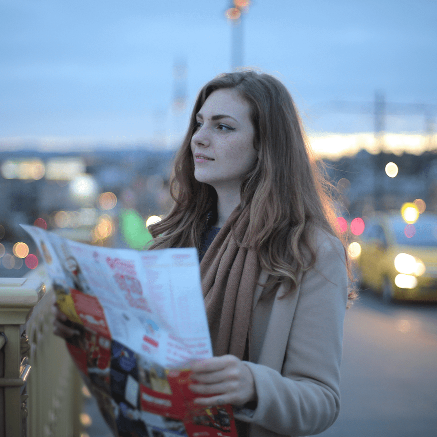 A woman holding a newspaper looks afar.