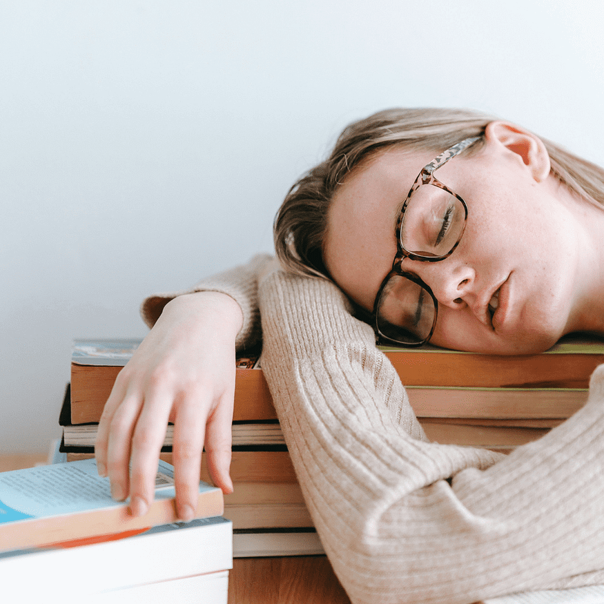 A woman resting her head, eyes closed, on a pile of books