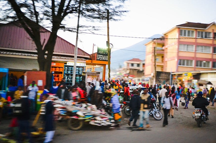 How To Build Systems Where The Rich DON’T Get Richer — A picture of a busy and bustling marketplace in Tanzania. There seem to be numerous businesses selling diverse things in this market, as the an impressive crowd visits the market.
