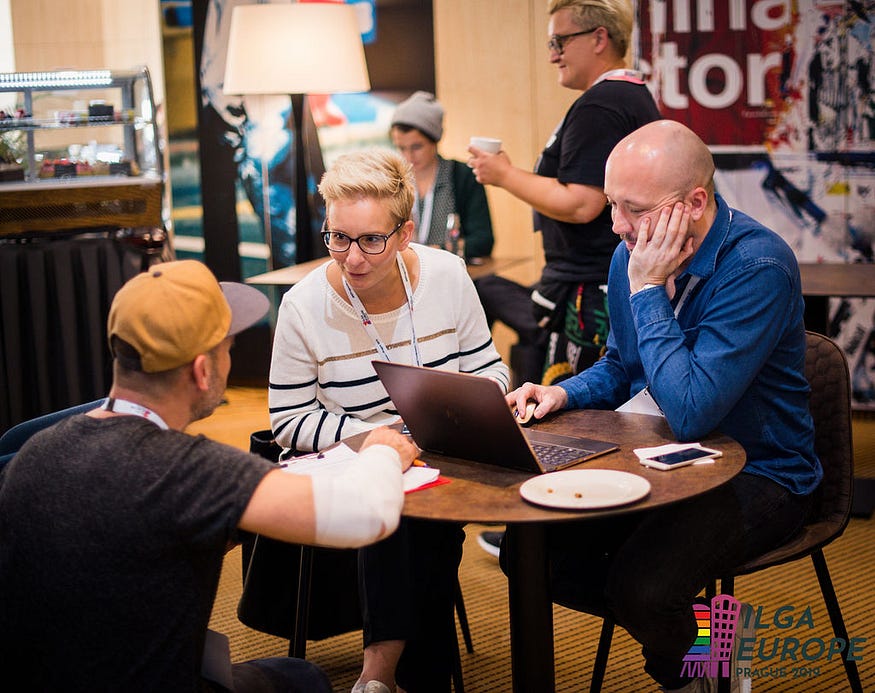 Three people talk around a coffee table.