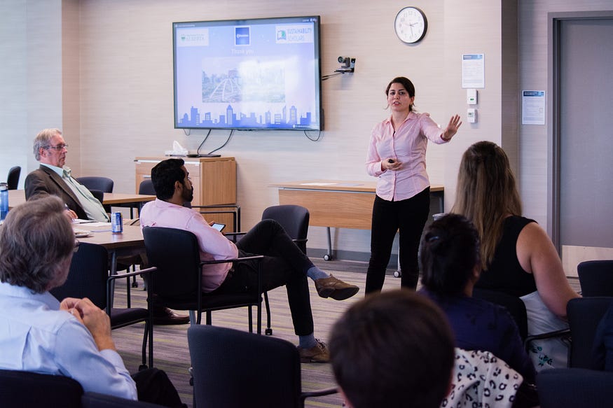 Woman in business casual speaks to a small room of attentive listeners.