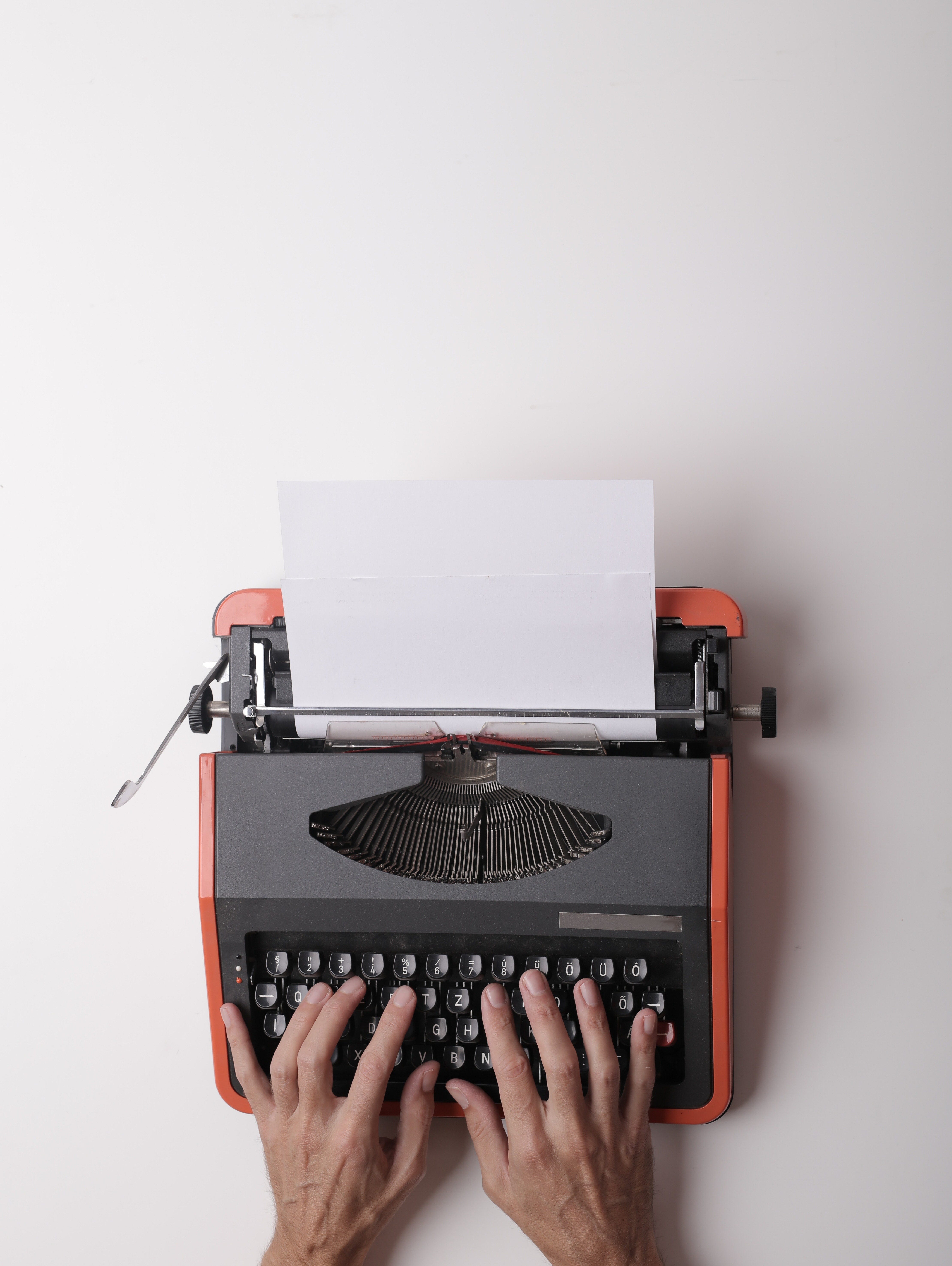 A typewritter in front of a white background with a pair of hands on top of it.