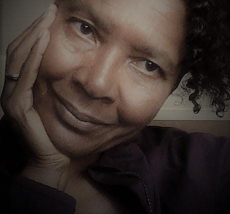A close-up of Valerie Haynes Perry; she has her hand on cheek. She wears a muted purple and stares peacefully at the camera.