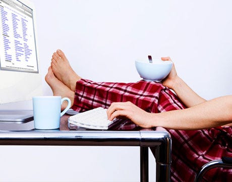Person in front of the computer, barefoot, in pajamas, with a coffee mug and bowl with a spoon