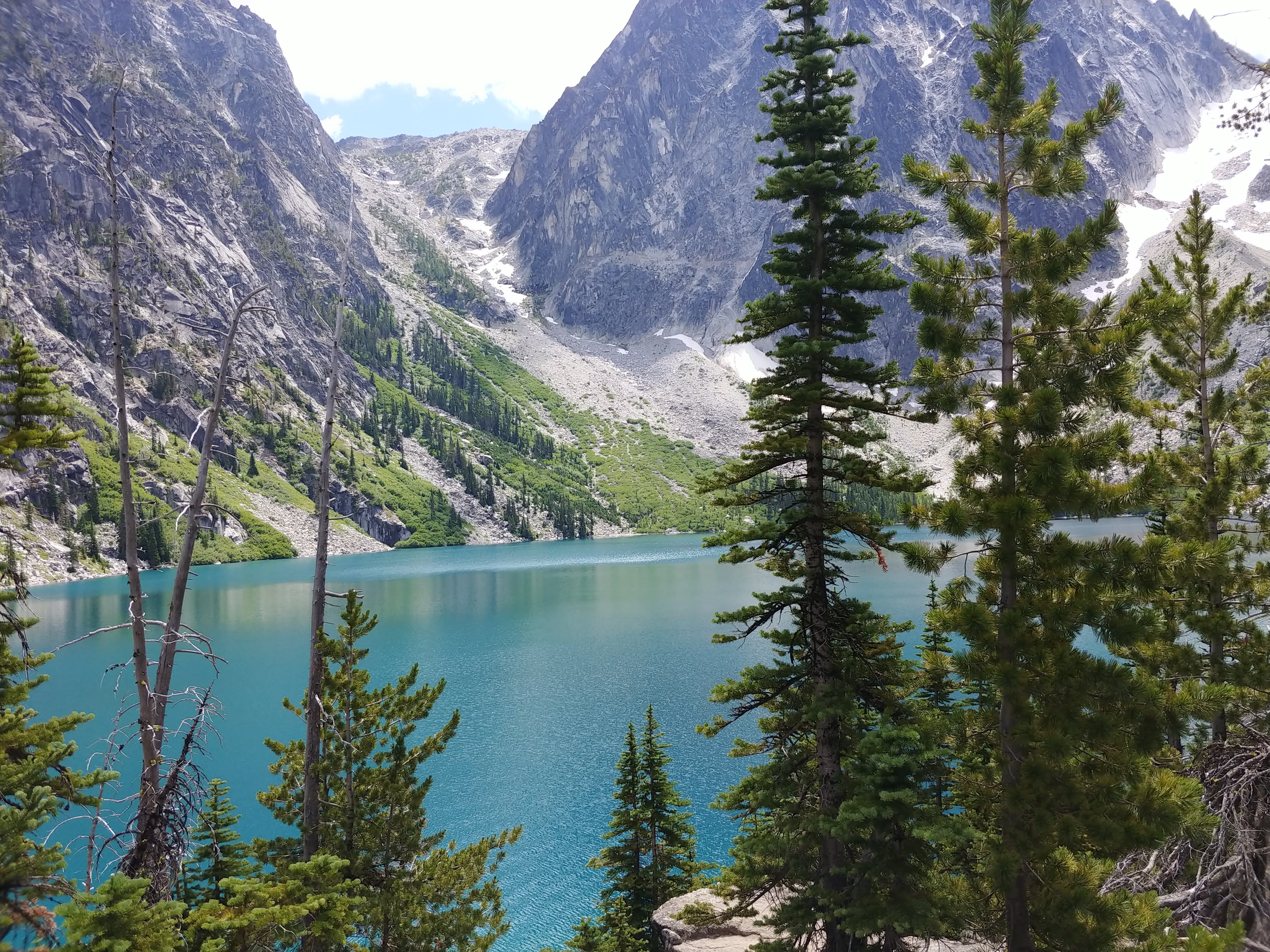 Colchuck lake, through sparse trees, with bare rock mountains behind; Apline Lakes Wilderness, Enchantments area, Washington.