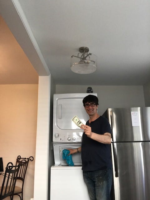 Author hold laundry in one hand and a dollar bill in another hand in front of a laundry machine.