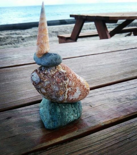 stones and shells stacked on each other on a wooden bench near the seashore