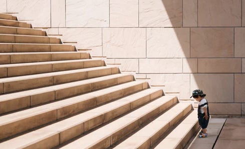 Photo: A little boy is looking at the first step of a long flight of stairs in front of him.