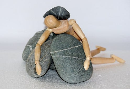 A drawing figurine is draped over a pile of rocks and also has a rock on it’s back.