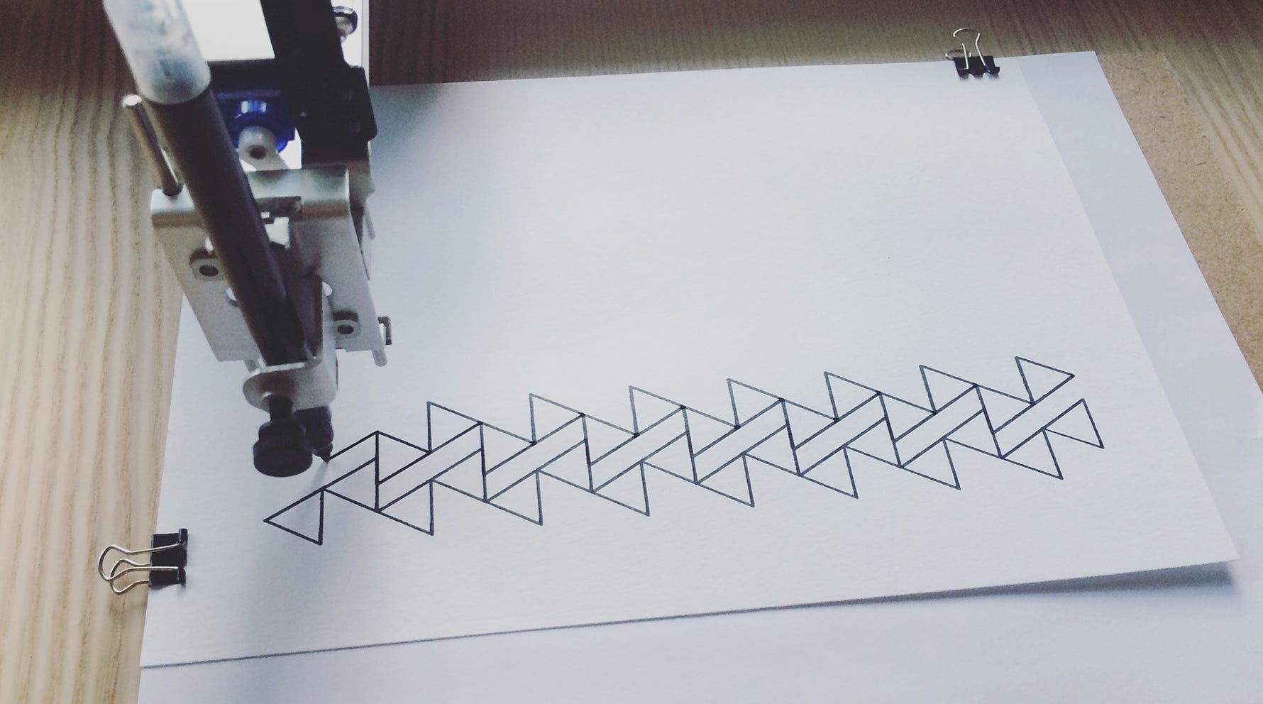 Photograph of a pen plotter by Matt Deslauriers. The image shows a pen plotter drawing interesting patterns with triangles.