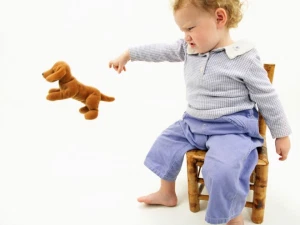 A toddler throwing away plush toy.