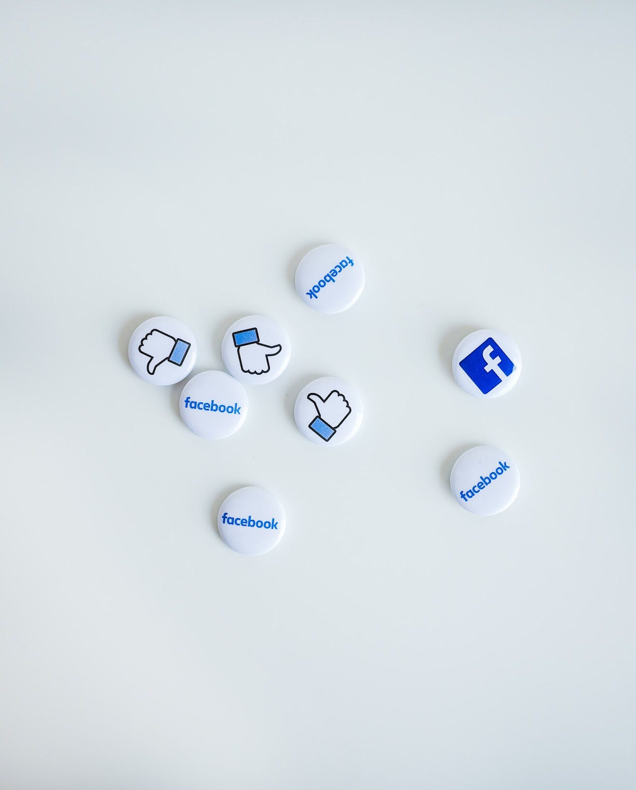 Various pins on a white table, all with Facebook symbols on them.