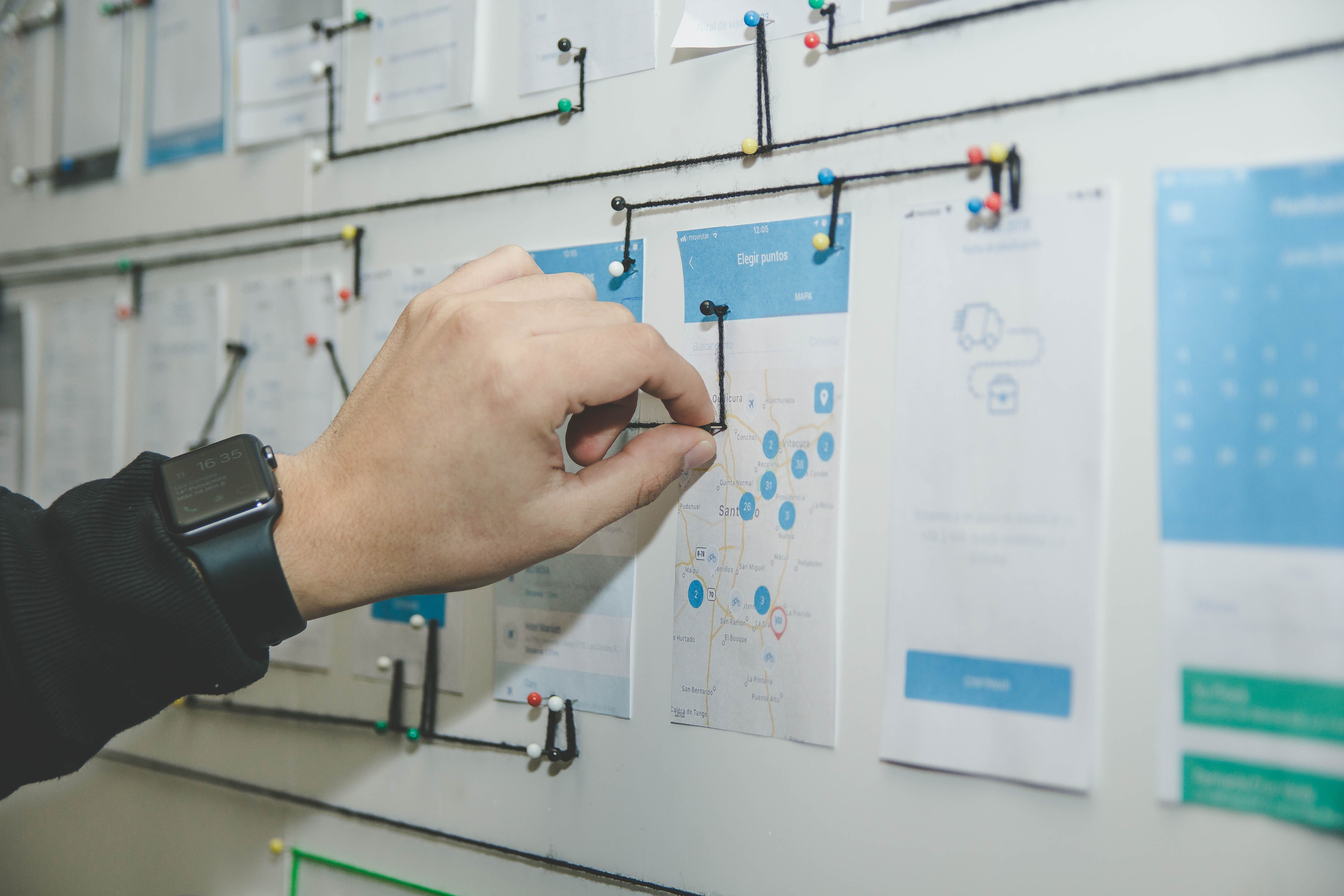 a person’s hand pinning up printed user flows to the wall