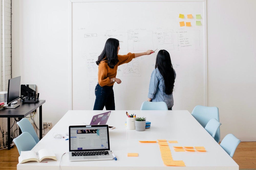 Two women standing at white board in conference room