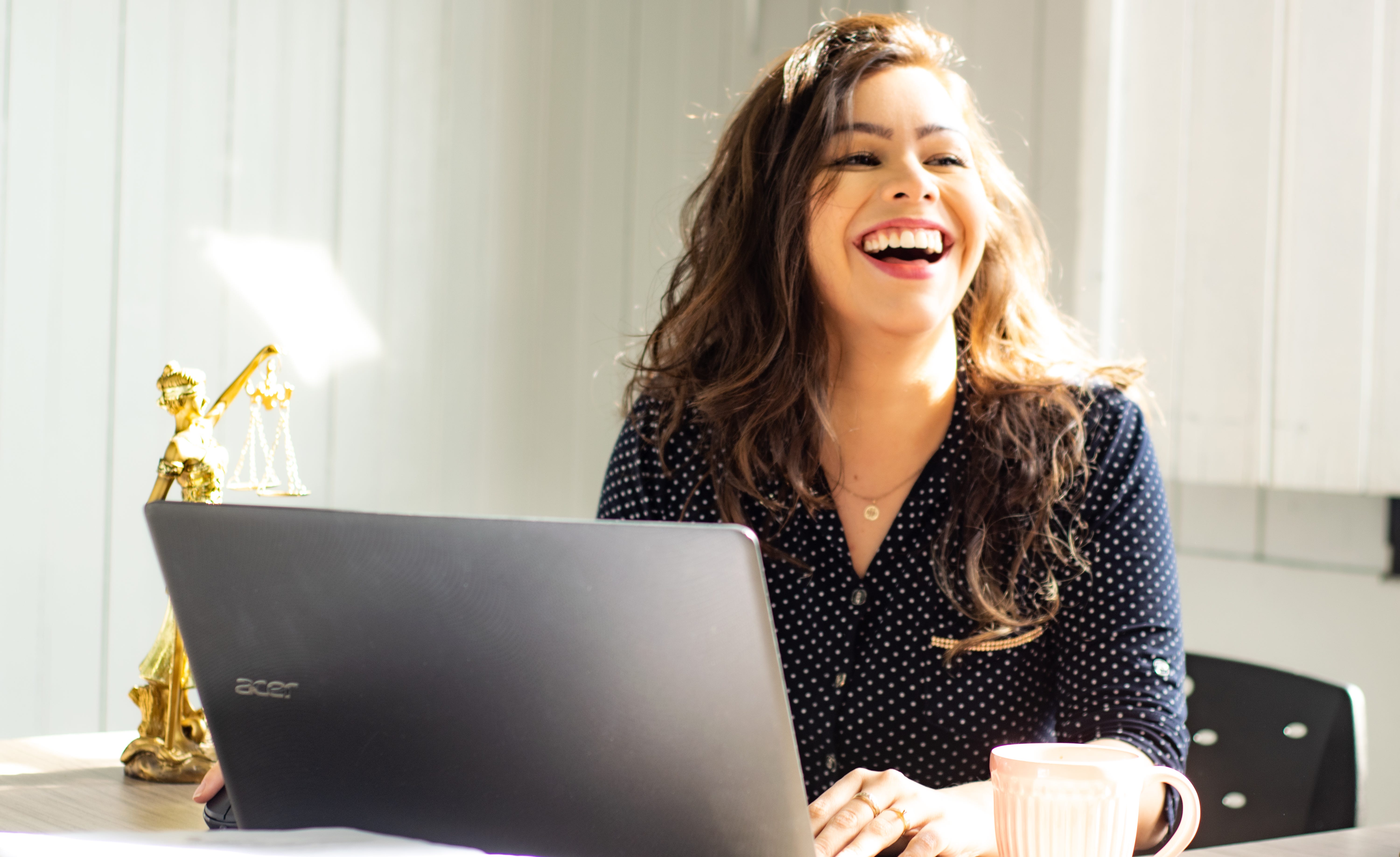 This is a photo of a person sitting at their desk with their laptop open and smiling widely.