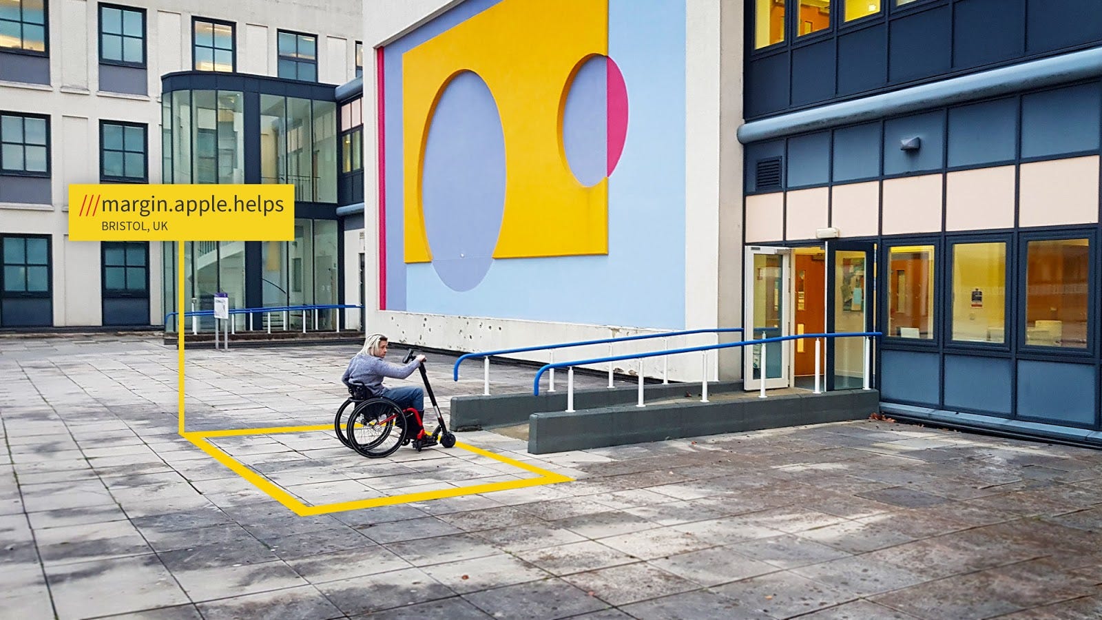 A person using a mobility scooter waits outside the accessible entrance of a colourful building in Bristol