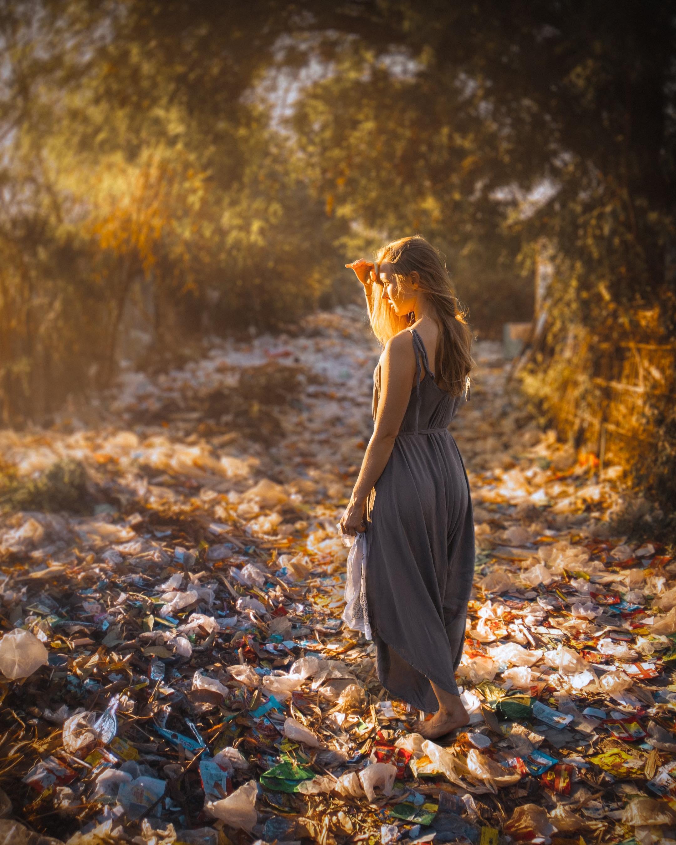 A woman stands in a trash filled pathway that looks like fallen leaves at first glance