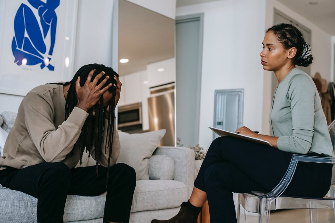 Overwhelmed black man discussing problem with female psychologist